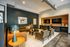 Modern living room with plush brown sofas, sleek armchairs, ambient lighting, and dual wall-mounted TVs in a stylish, cozy setting.
