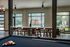 Chic communal lounge with pool table, modern seating, and floor-to-ceiling windows overlooking lush greenery and outdoor BBQ area.