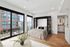 Elegant bedroom with large windows showcasing urban views, featuring a stylish bed, wooden flooring, and modern decor.