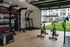 Modern home gym with natural light, featuring exercise bikes, punching bag, and free weights, opening to a lush green outdoor space.