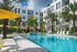 Luxurious apartment complex featuring a sparkling pool surrounded by elegant palm trees and bright yellow umbrellas, offering a tropical oasis feel.
