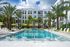 Luxurious apartment complex with a stunning tropical pool area, surrounded by palm trees and stylish lounge chairs under vibrant yellow umbrellas.