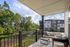 Charming balcony with cozy seating offers a serene view of lush greenery and modern apartment buildings under a clear blue sky.