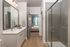 Modern bathroom design featuring a sleek vanity with large mirror, elegant glass shower, and glimpse into a cozy, well-lit bedroom.