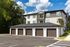 Modern apartment building with elegant siding and attached garages, surrounded by lush greenery and a clear blue sky.