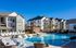Luxurious apartment complex with a stunning outdoor pool and modern lounge area, surrounded by beautiful, multi-story residential buildings under a clear blue sky.