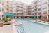 Luxurious apartment complex featuring a pristine pool surrounded by stylish loungers and vibrant teal umbrellas, offering a perfect urban oasis.