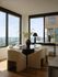 Modern dining area with elegant furnishings, featuring a round table and chic beige chairs, surrounded by large windows offering breathtaking city views.