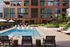 Luxurious apartment building with a sparkling outdoor pool, surrounded by lush greenery and modern seating areas, perfect for relaxation and leisure.