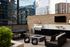 Luxurious rooftop patio with modern outdoor kitchen, grill, lounge seating, and string lights against a city skyline backdrop.