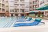 Luxurious apartment complex pool area with stylish loungers, vibrant green umbrellas, and modern building backdrop.