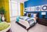 Vibrant bedroom with bold blue accent wall, stylish art, and lush green curtains offering a cozy atmosphere.