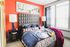 Vibrant modern bedroom with a bold orange accent wall, stylish geometric headboard, and colorful bedding, complemented by large windows for natural light.