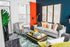 Vibrant living room with a stylish gray sofa, colorful cushions, and a bold striped armchair, enhanced by large abstract art and rich, orange curtains.