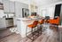 Bright and modern kitchen with sleek grey cabinets, stainless steel appliances, and a spacious island with vibrant orange stools. Cozy living area with contemporary decor and ample natural light.