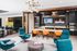 Modern apartment lounge with vibrant teal armchairs, stylish orange dining chairs, and a sleek black kitchen featuring dual TVs and sophisticated lighting.