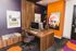Vibrant contemporary office space featuring a wooden desk with modern chairs, decorative wall art including a colorful portrait, and bold orange accents.