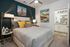Elegant bedroom featuring a cozy bed with vibrant yellow cushions, modern art, and a chic ensuite bathroom.