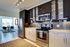 Modern kitchen with sleek stainless-steel appliances, chic dark cabinetry, and elegant tile backsplash, opening to a bright dining area.