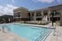 Luxurious apartment complex with a sparkling outdoor pool, surrounded by cozy lounge chairs and modern architecture under a clear blue sky.