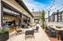 Charming outdoor patio of a modern apartment, featuring cozy seating areas, vibrant flowers, and sleek string lights against a clear blue sky.