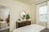 Elegant bedroom featuring a stylish dresser with a round mirror, lush indoor plant, and cozy bed in a bright, sunlit space.