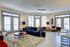 Elegant, sunlit living room with plush blue sofa, cozy rug, and modern decor, featuring large windows and stylish lighting.
