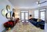 Elegant living room with a cozy blue sofa, stylish gold wall art, and abundant natural light streaming through large windows.