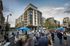 Vibrant urban scene with a modern apartment building, lively outdoor event, and bustling atmosphere.