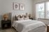 Charming bedroom with elegant decor, featuring a plush bed, stylish lamps, artistic wall prints, and abundant natural light through large windows.