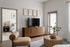 Inviting living room with modern furniture, a sleek TV console, cozy armchair, and stylish coffee table. Bright bedroom visible through an open doorway, enhancing the apartment's airy ambience.
