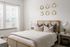 Bright and elegant bedroom with stylish wooden accents, cozy bedding, and soft natural light from large windows.