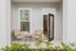 Charming outdoor patio with wicker chairs, a cozy table, and lush greenery, leading into a bright, inviting apartment interior.