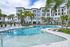 Luxurious apartment complex featuring a beautiful outdoor pool surrounded by lush palm trees and modern lounge chairs, perfect for relaxation.