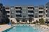 Elegant apartment building with balconies overlooking a pristine swimming pool, surrounded by lush landscaping and modern lounge chairs.
