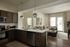 Modern, open-concept kitchen with sleek countertops, stylish pendant lights, and a cozy living area view. Natural light floods through large windows, highlighting contemporary furnishings.