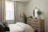 Bright and inviting bedroom with a large window, elegant beige curtains, and a stylish wooden dresser adorned with contemporary decor and a circular mirror.