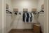 Pristine walk-in closet showcasing ample storage space with organized hanging clothes, sleek black hangers, and woven baskets.
