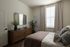 Inviting bedroom with natural light, featuring elegant decor, a plush bed with textured pillows, and a rustic wooden dresser topped with greenery.