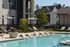 Inviting luxury apartment complex with a sparkling outdoor pool, stylish lounge chairs, and lush landscaping under the clear blue sky.