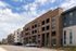 Contemporary brick apartment building with multiple floors, ample parking, and modern design under a bright blue sky.
