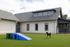Charming modern farmhouse with sleek gray siding, lush green lawn, and playful outdoor space featuring a colorful slide, ideal for pets and family fun.