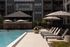 Luxurious apartment complex featuring a sparkling pool with chic lounge chairs, shaded by elegant umbrellas, perfect for relaxation.