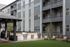 Contemporary apartment exterior with private balconies, lush green courtyard, and stylish outdoor grilling area.