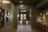 Elegant hallway with sophisticated decor featuring framed art, warm wood paneling, and inviting lighting leading to a contemporary sitting area with natural light and modern furniture.