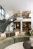 Elegant living space with plush green sectional, modern lighting, and a stylish open staircase leading to an airy loft.
