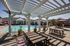Inviting outdoor pool area with pergola-shaded seating, modern loungers, and lush poolside greenery under a clear blue sky.
