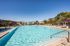 Luxurious apartment complex pool with pristine water, surrounded by palm trees and stylish lounge chairs under a clear blue sky.