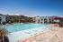 Luxurious apartment complex showcasing a sparkling pool with stylish sun loungers, elegant pergola, and lush tropical landscaping under a bright blue sky.