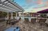 Charming outdoor pool area with modern lounge chairs, lush landscaping, and a serene waterfall feature under a beautiful sunset sky.
